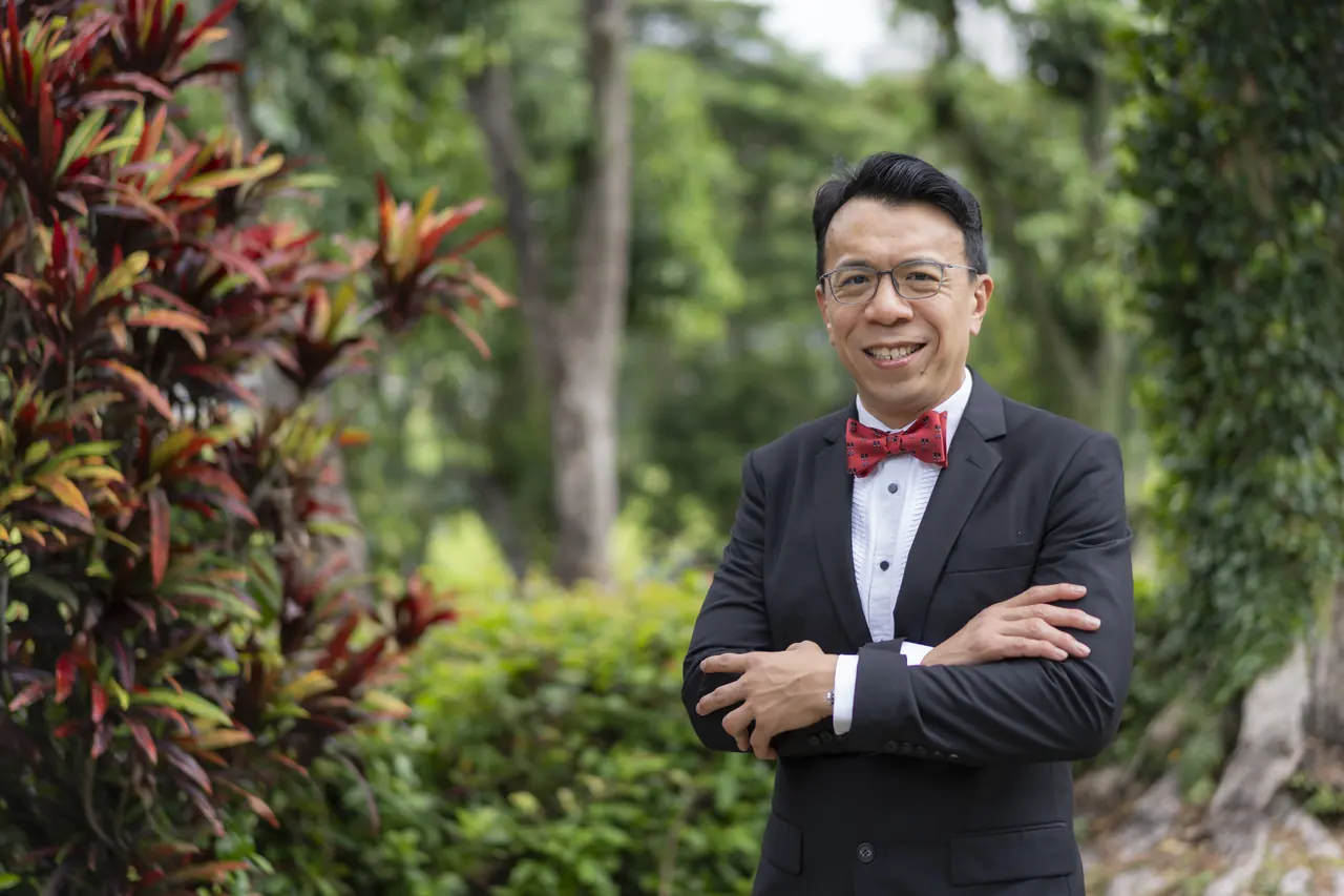 Dr Lai Kah Weng, standing outdoors in a dark suit and red bow tie